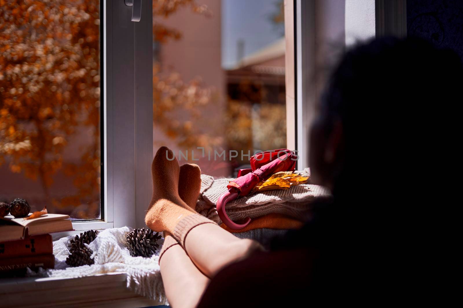 A cozy autumnal day. A woman hanging her legs on the window sill. Cold autumn sunny day. Drink coffee near the window