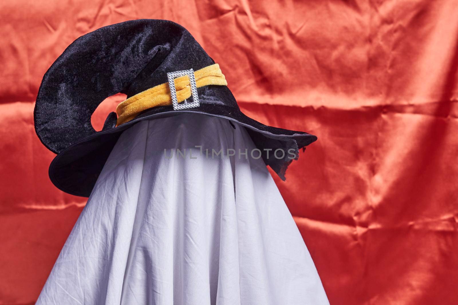 White ghost on orange. Halloween holiday. A young child dressed in a ghost costume for Halloween on orange background. Funny Halloween kid. Little cute child in white costume and sunglasses