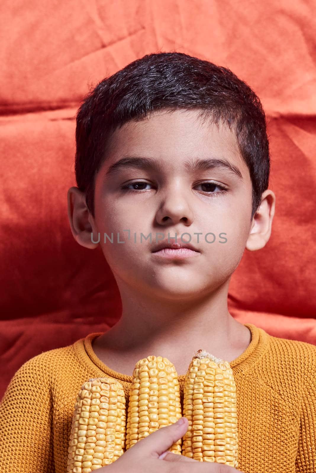 A little boy holds raw corns over orange background