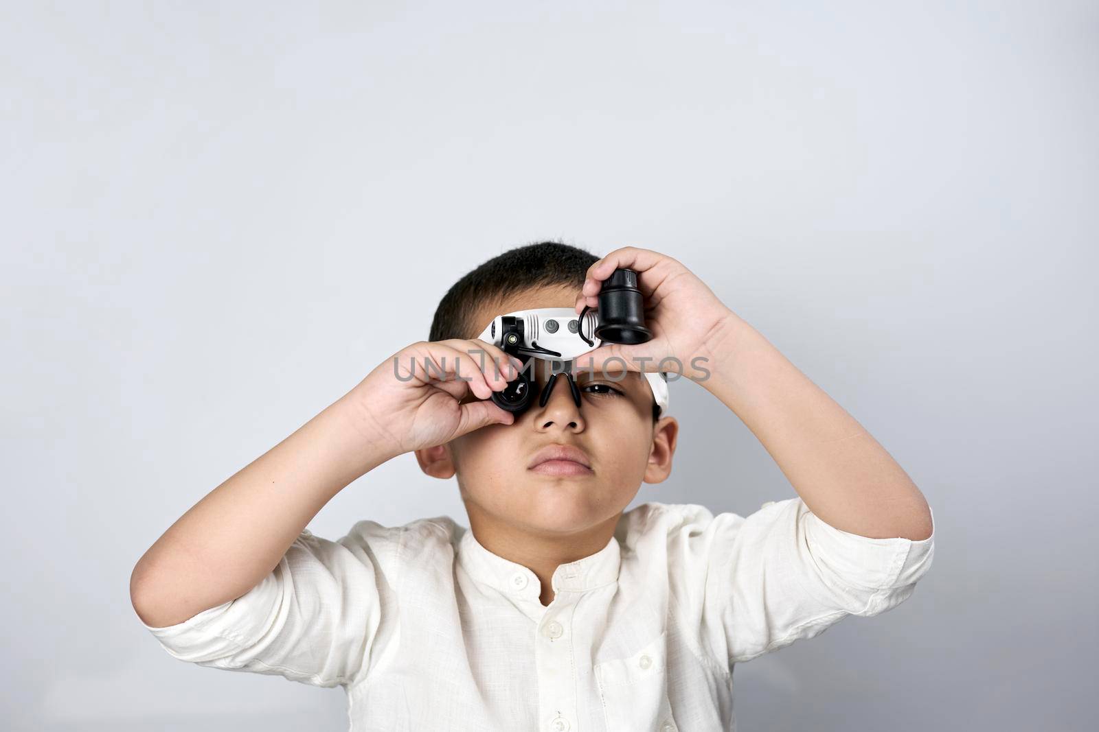A multiethnic boy in magnifying eyeglasses against the white table