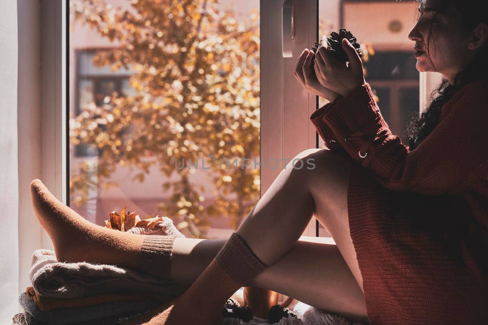 Cold autumn days - a young multi-racial female drinks coffee in a cozy windowsill. Middle-eastern or mixed-race woman enjoys weekend drinking hot tea near the windows