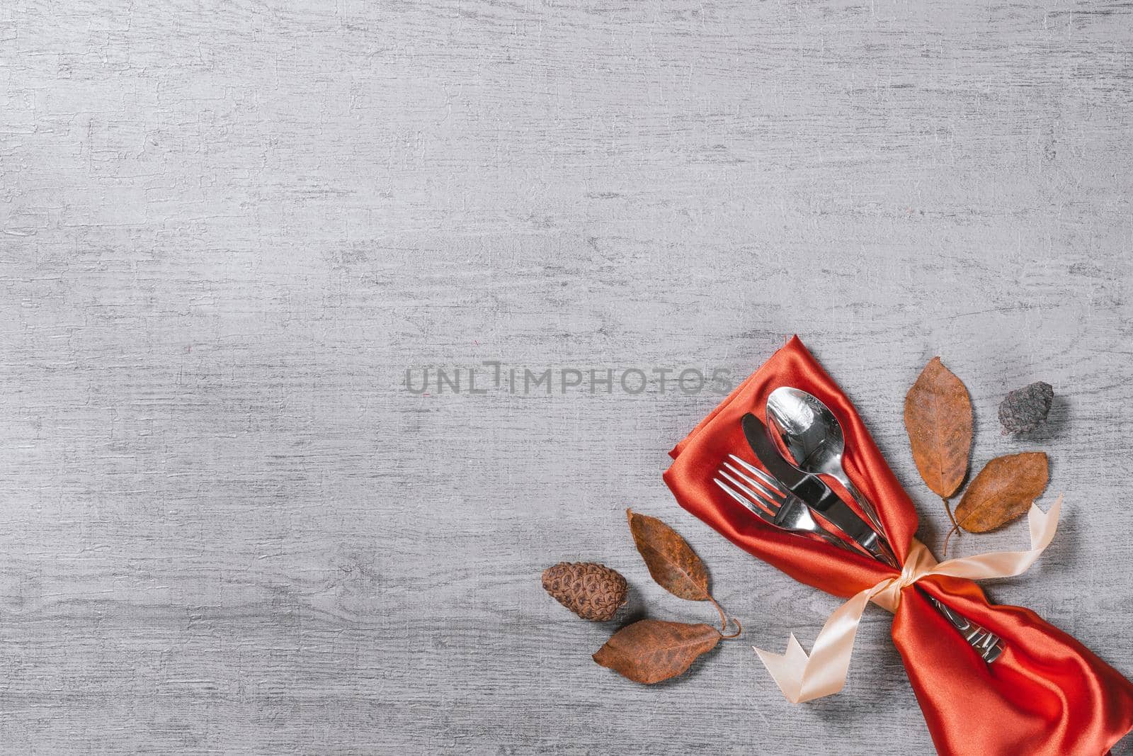 Set of cutlery set with red silk napkin and fall leaves on wooden background with copy space. Autumnal concept backgorund for cafe and restaurants
