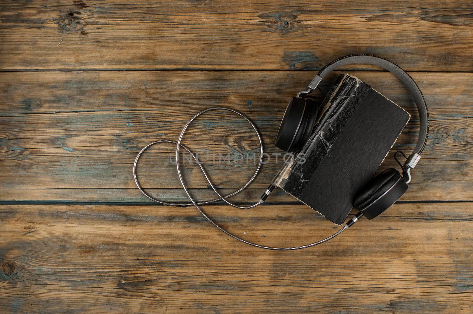 Audio book concept. Headphones and old book over wooden table. Top view with space for your text by inxti