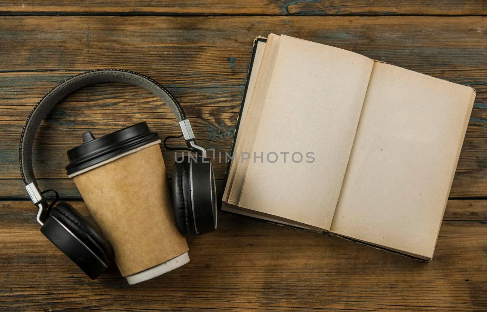 Open book  with blank page headphone and a cup of coffee in a disposable paper cup on a wooden table. Remote education concept. Top view by inxti