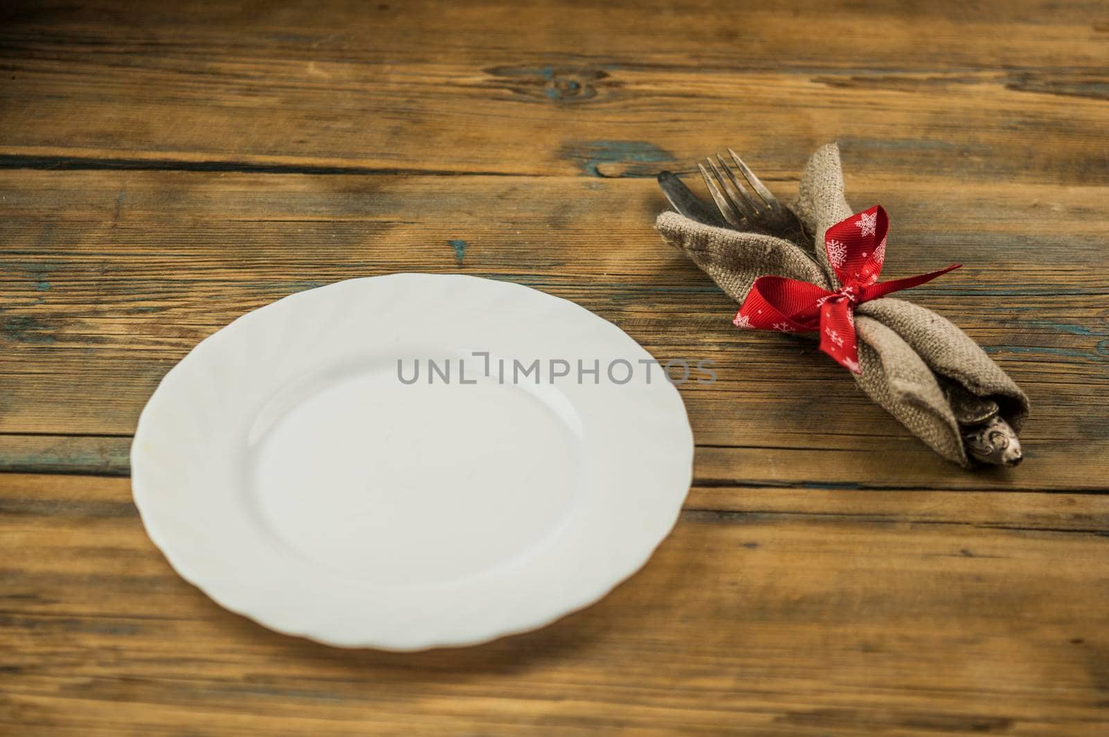 Festive composition with empty white plate and cutlery set on rustic wooden table. Christmas holiday.