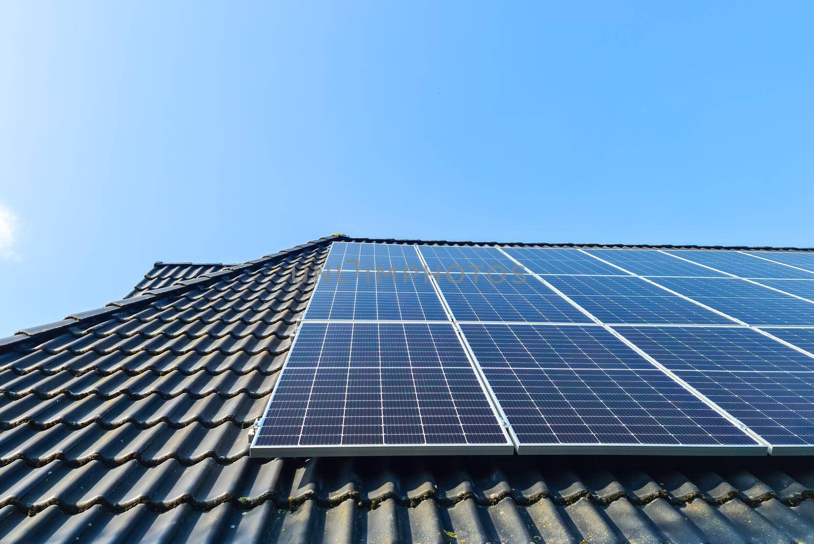 Solar panels producing clean energy on a roof of a residential house with black roof tiles