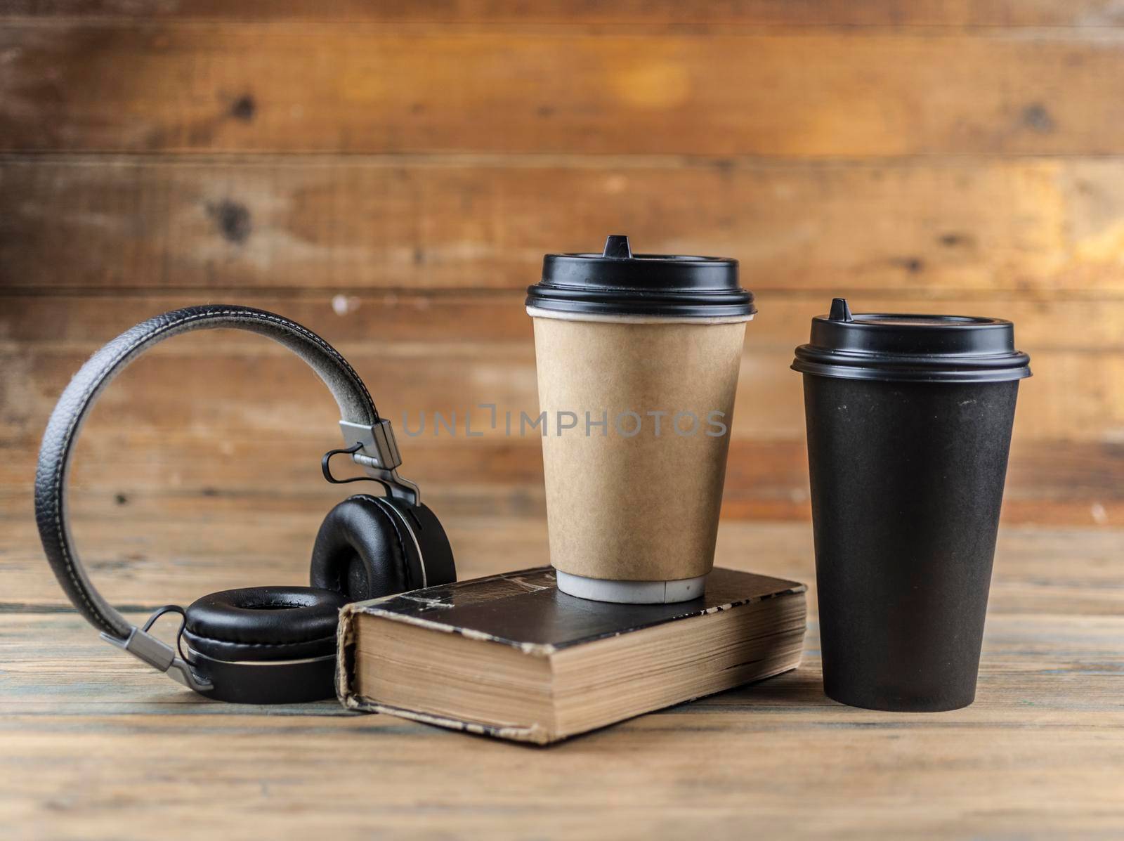 old book with headphone and a cup of coffee in a disposable paper cup on a wooden table. Remote education concept. 