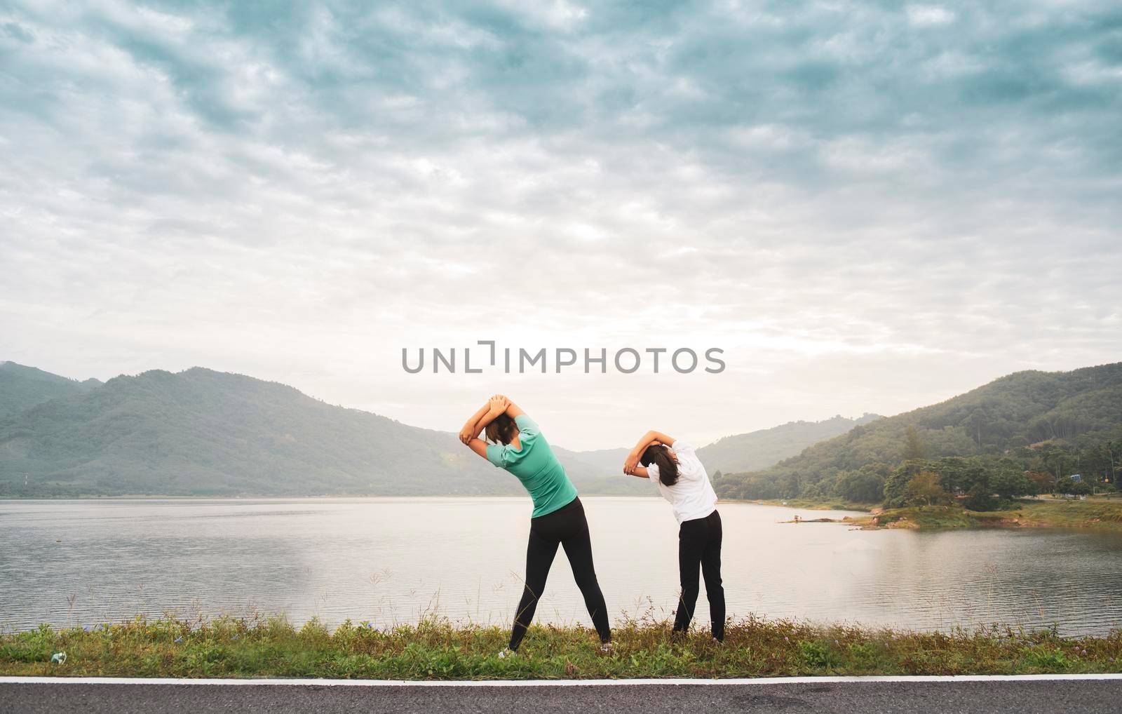 Mom and girl child doing stretching before workout outdoor at mountain lake in the morning to get a healthy lifestyle. by thanumporn