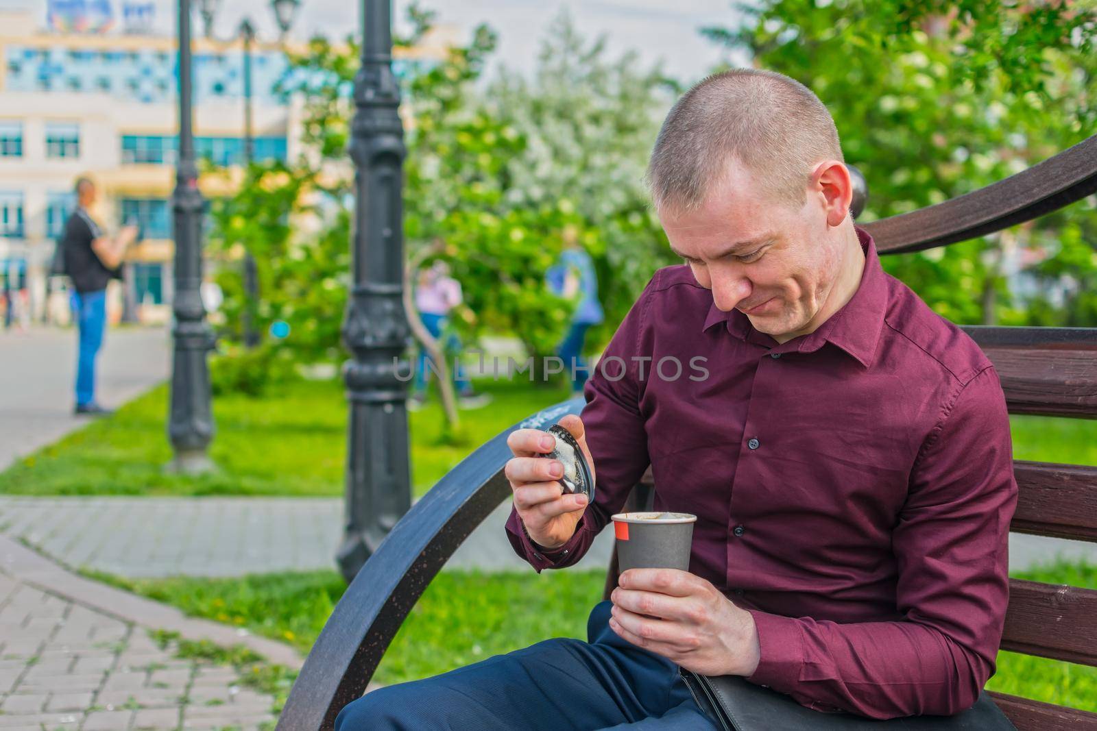 Joyful office worker opening a delicious and hot drink during lunch while sitting on a park bench