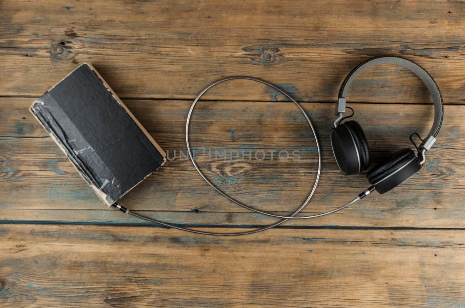 Audio book concept. Headphones and old book over wooden table. Top view with space for your text. Remote education concept.
