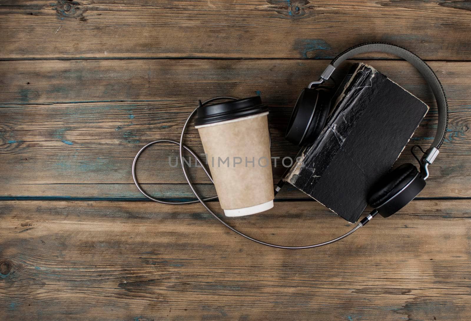 old book with headphone and a cup of coffee in a disposable paper cup on a wooden table. Remote education concept.  by inxti