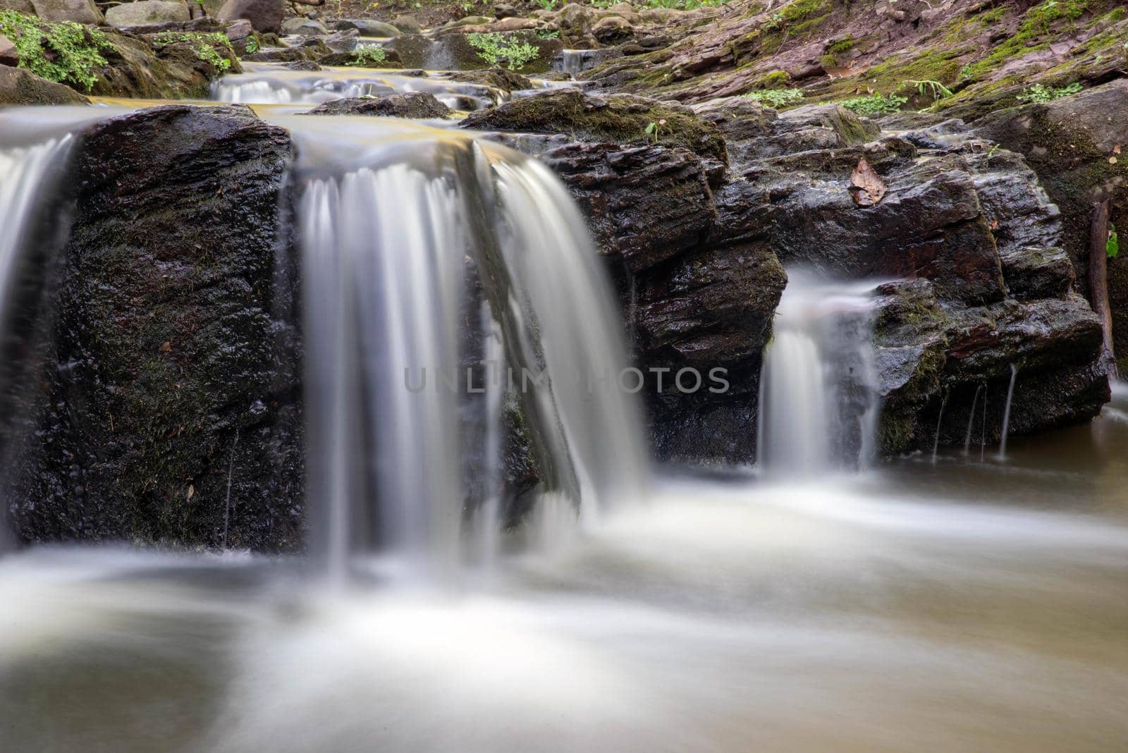Closeup long exposure of soft woodland waterfall cascading over rocks by marysalen