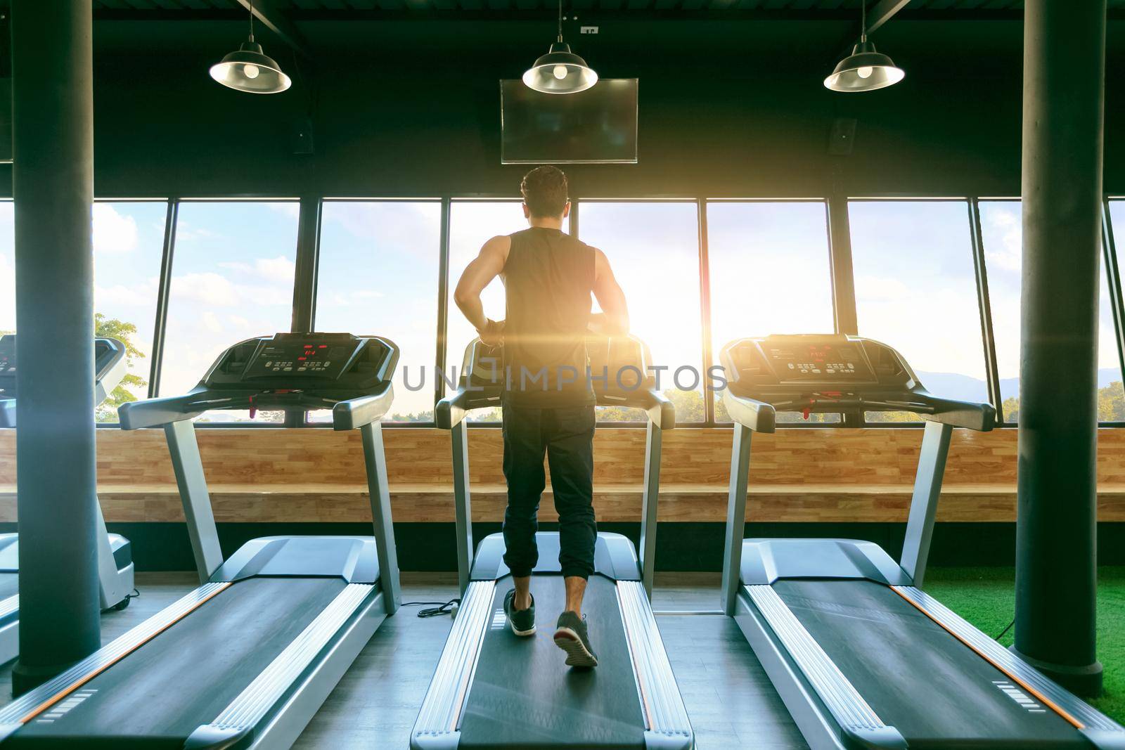 Back view of young man athlete with running on treadmill in gym.