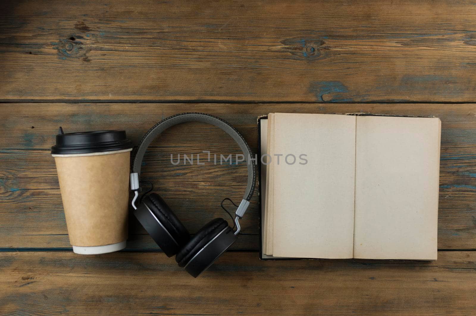 Open book with blank page, headphone and a cup of coffee in a disposable paper cup on a wooden table. Remote education concept. Top view