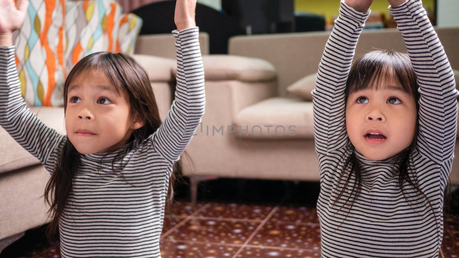 Little cute girls practicing yoga pose on a mat indoors. Little children doing exercises on blue yoga mat at home. Happy Asian sisters spending time together on vacation.