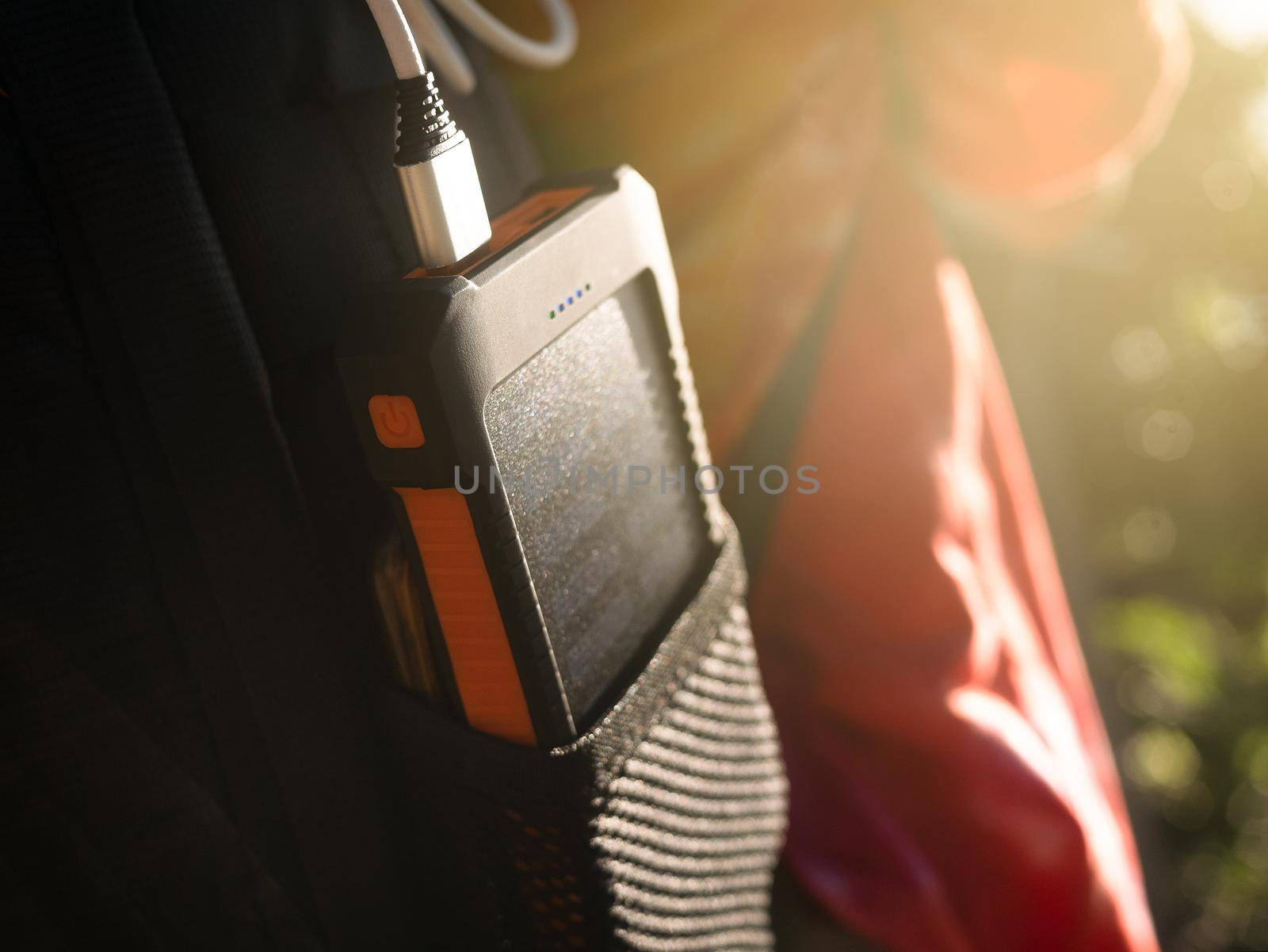 A rechargeable mobile power pack with solar panels in young female traveler's backpack, close-up. Connected to and charging a mobile, tablet or smart phone. by TEERASAK