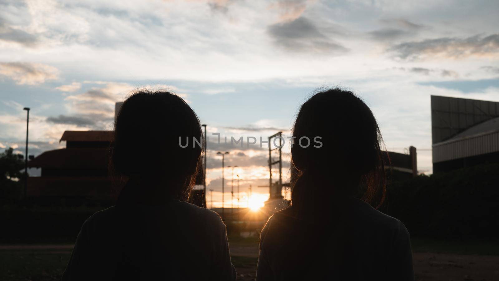 Two sibling sisters eating sweet tasty ice cream outdoors at sunset. Two happy young kid enjoy dessert during vacation holiday in the park. by TEERASAK