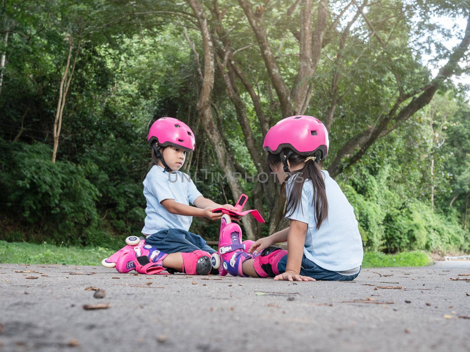 Cute older sister is helping younger sister to put on a protection pads and safety helmet practicing to roller skate on the street in the park. Active outdoor sport for kids.