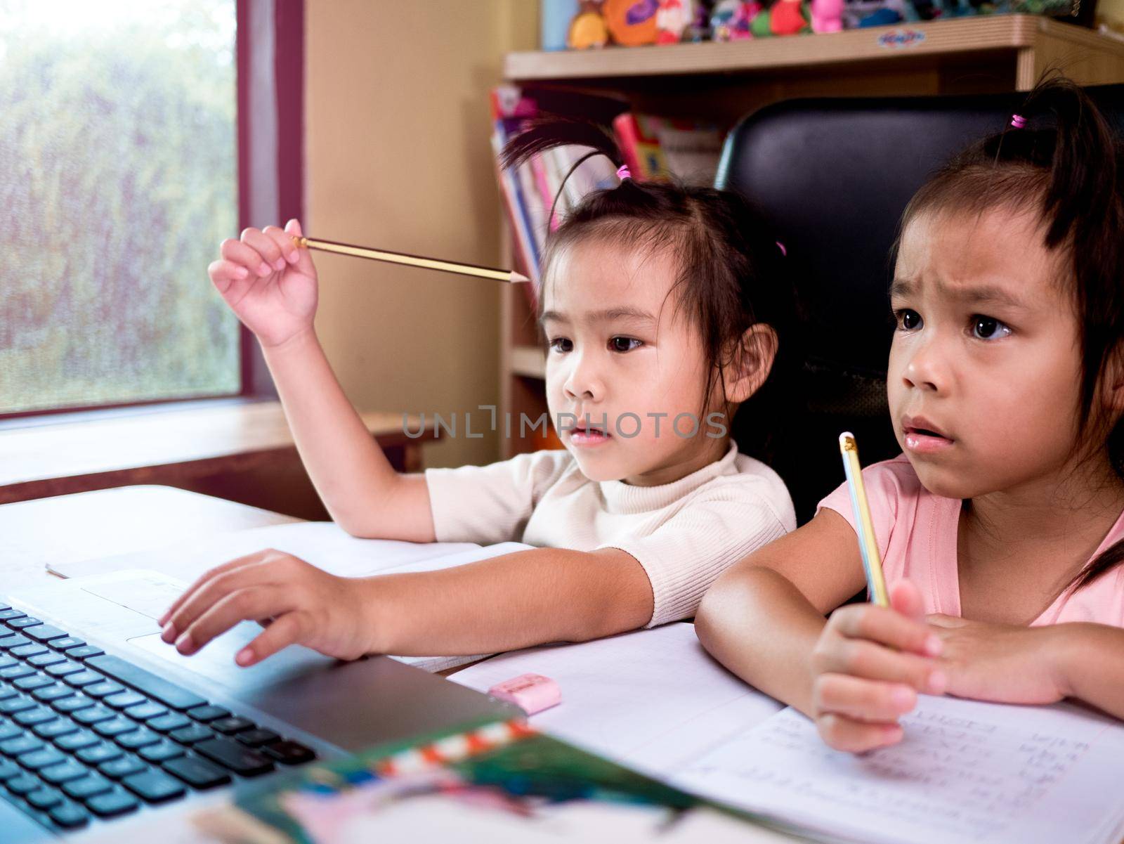 Two little schoolgirls studying homework math during her online lesson at home, social distancing during the coronavirus outbreak. Concept of online education or home schooler. by TEERASAK