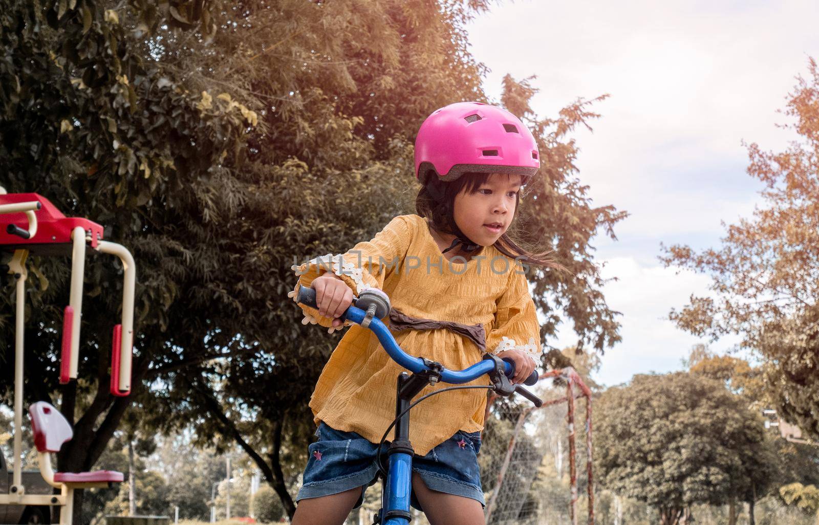 Cute little girl in safety helmet having fun with a balance bike in summer park. Outdoor sports for kids. childhood happiness. by TEERASAK