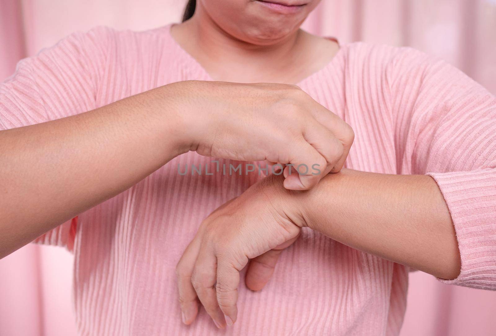 Annoyed middle-aged woman scratching itch on her arm from itchy dry skin, eczema, dermatitis, allergy, psoriasis. Health care and skin disease concept. by TEERASAK