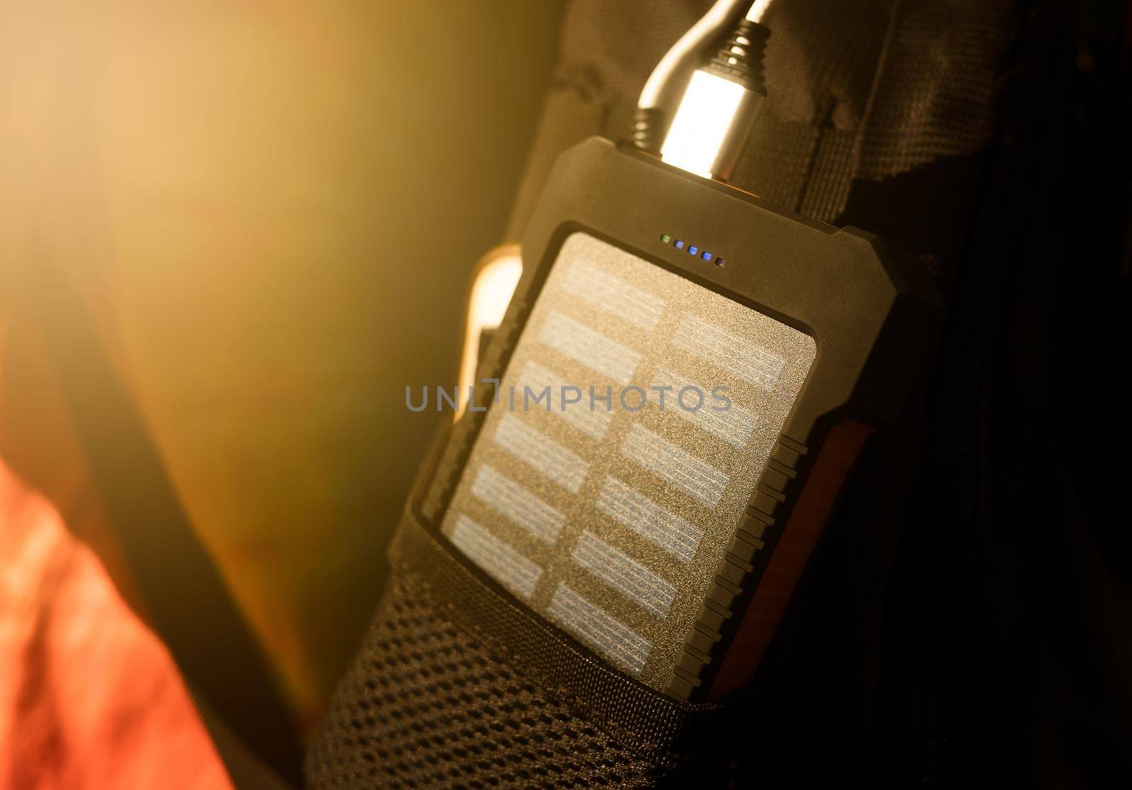 A rechargeable mobile power pack with solar panels in young female traveler's backpack, close-up. Connected to and charging a mobile, tablet or smart phone. by TEERASAK
