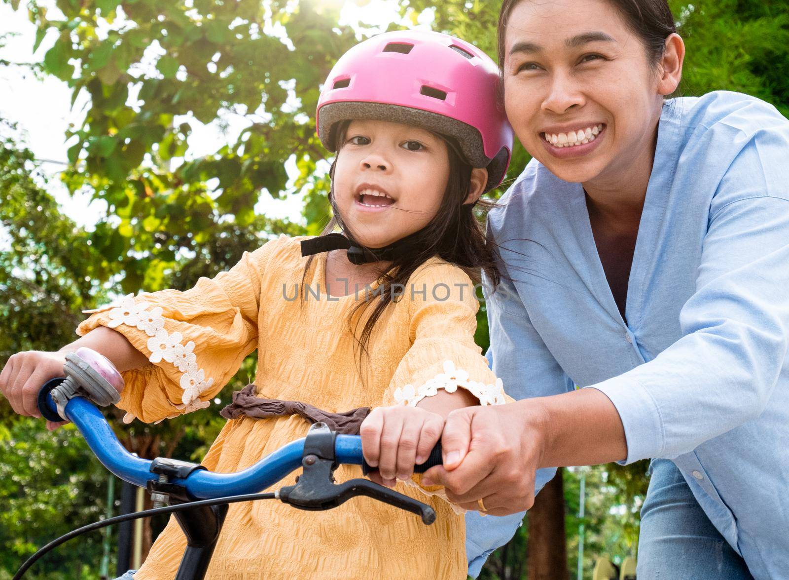 Cute little girl in safety helmet learn to ride a bike with her mother in summer park. Outdoor sports for kids. childhood happiness. family spending time together.