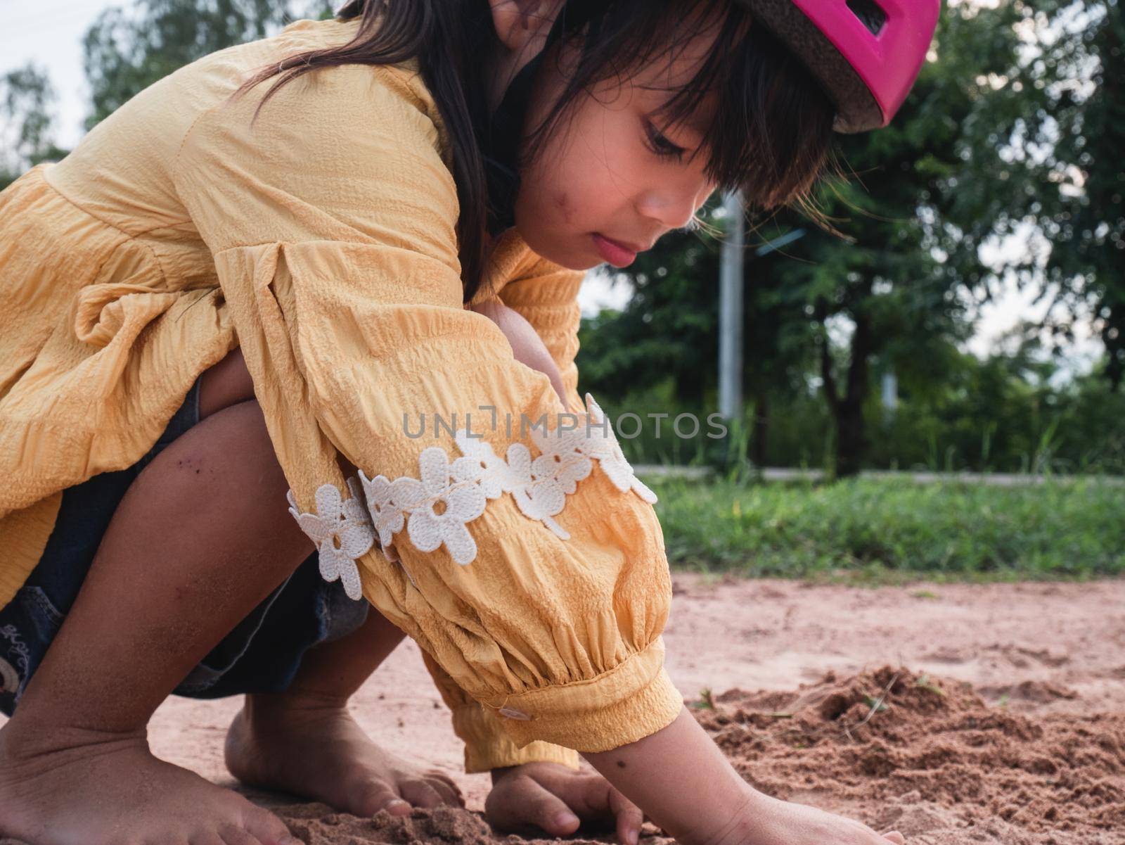Cute little girl in helmets are playing with sand in park on a sunny summer day, taking a break after cycling practice. develop imagination and exploration.