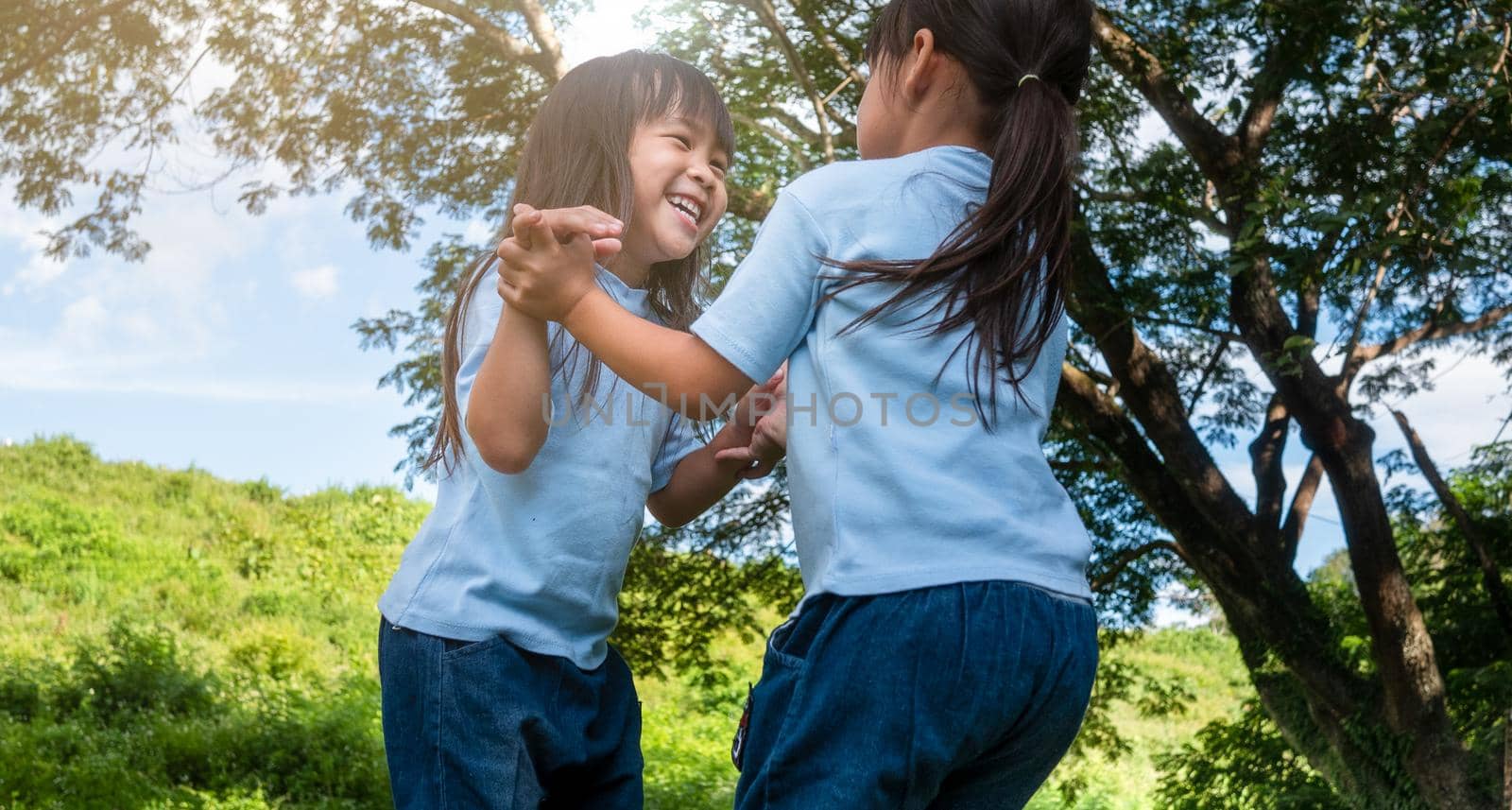 Two sibling little girls laughing and hugging each other on warm and sunny summer day in the garden. Young girls with her mother spending day in park. by TEERASAK