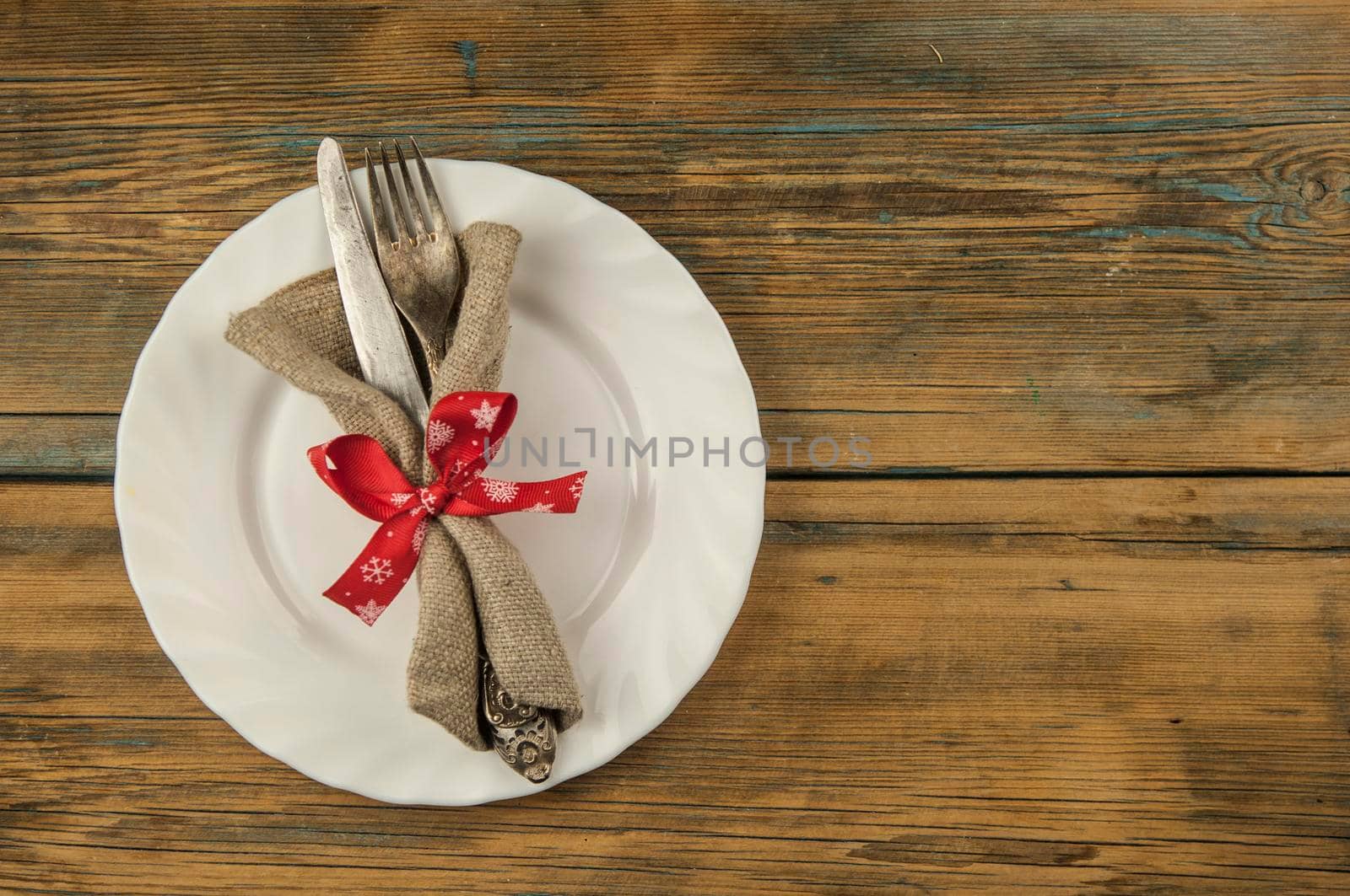 Festive composition with empty white plate and cutlery set on rustic wooden table. Christmas holiday. Top view