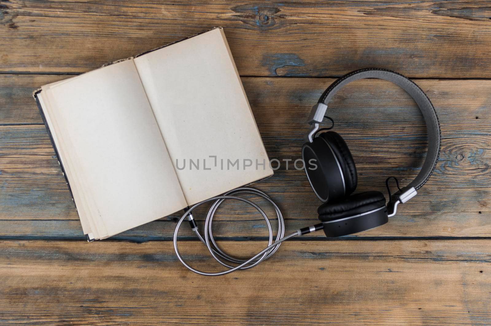 Open book with blank page and headphones on a wooden table. Remote education concept. Top view
