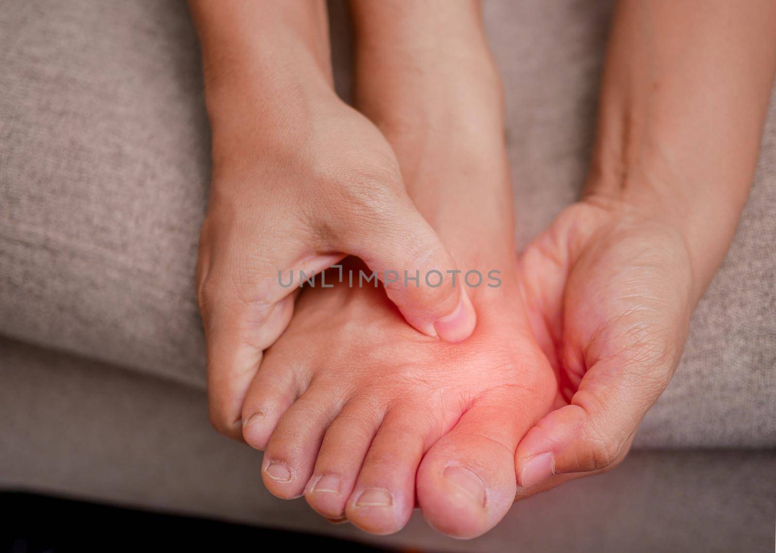 Closeup of female holding her painful feet and massaging her bunion toes to relieve pain. Swollen bunion at the edge of the big toe causes deformity (Hallux valgus). Woman's health concept. by TEERASAK