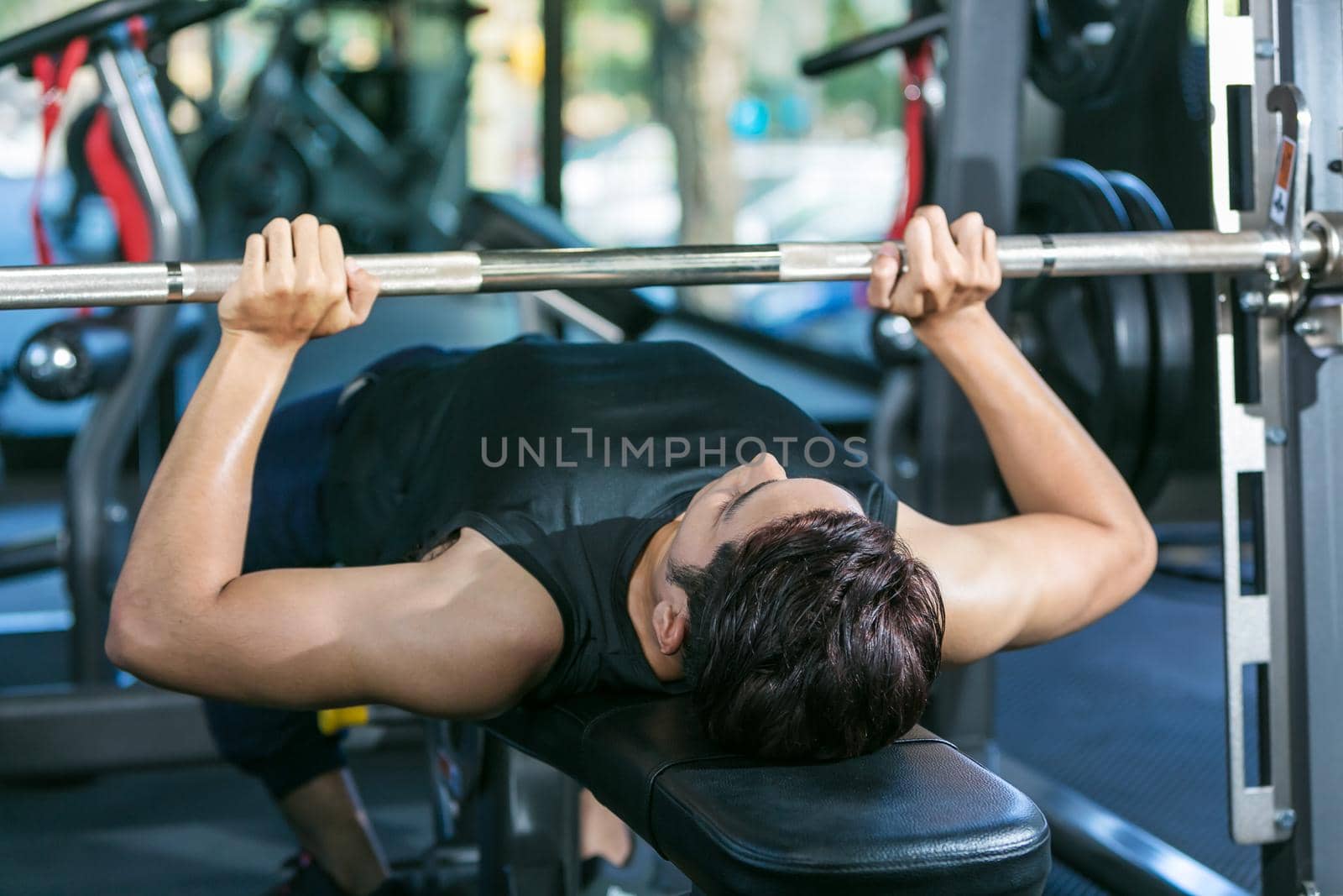 Man lifting dumbbell weights while lying down in gym.