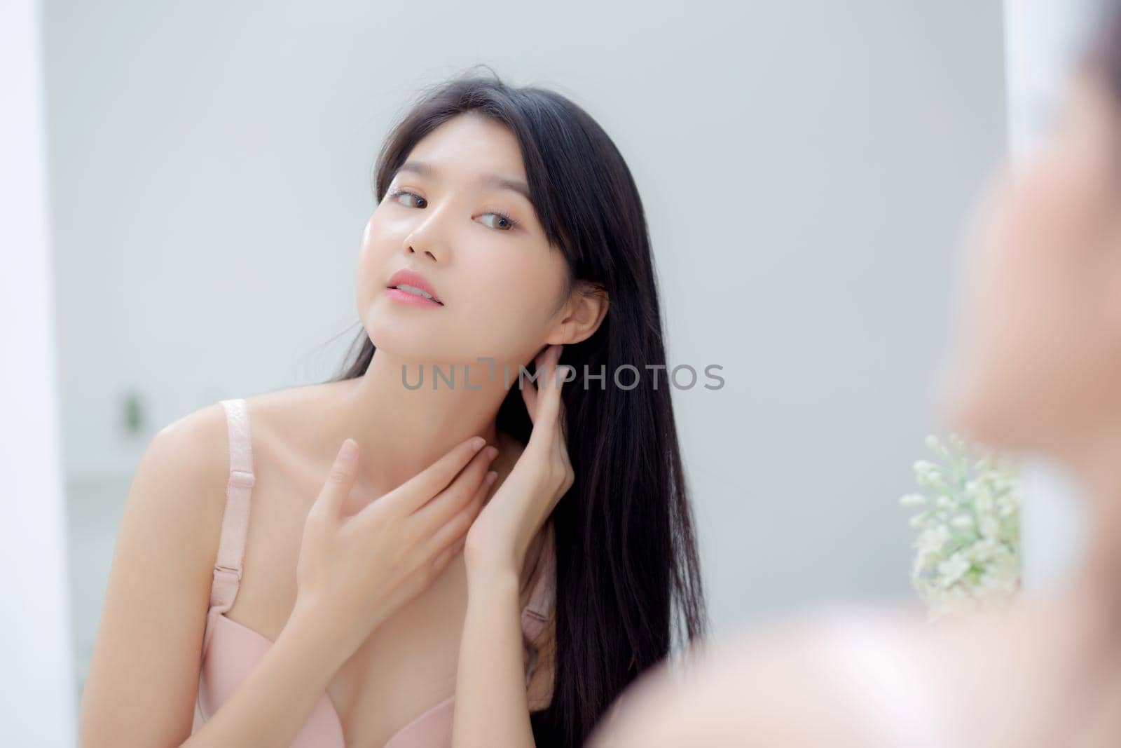 Beautiful sexy young asian woman looking mirror applying cream on neck and message, beauty girl applying body lotion skin care for health and soft hydration, treatment and cosmetic with moisturizer. by nnudoo
