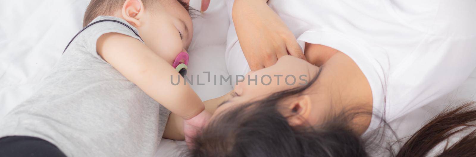 Young asian mother touch head of little baby girl with tender on bed in the bedroom, mom love newborn and care, woman with expression with child together, parent and daughter, family concept.