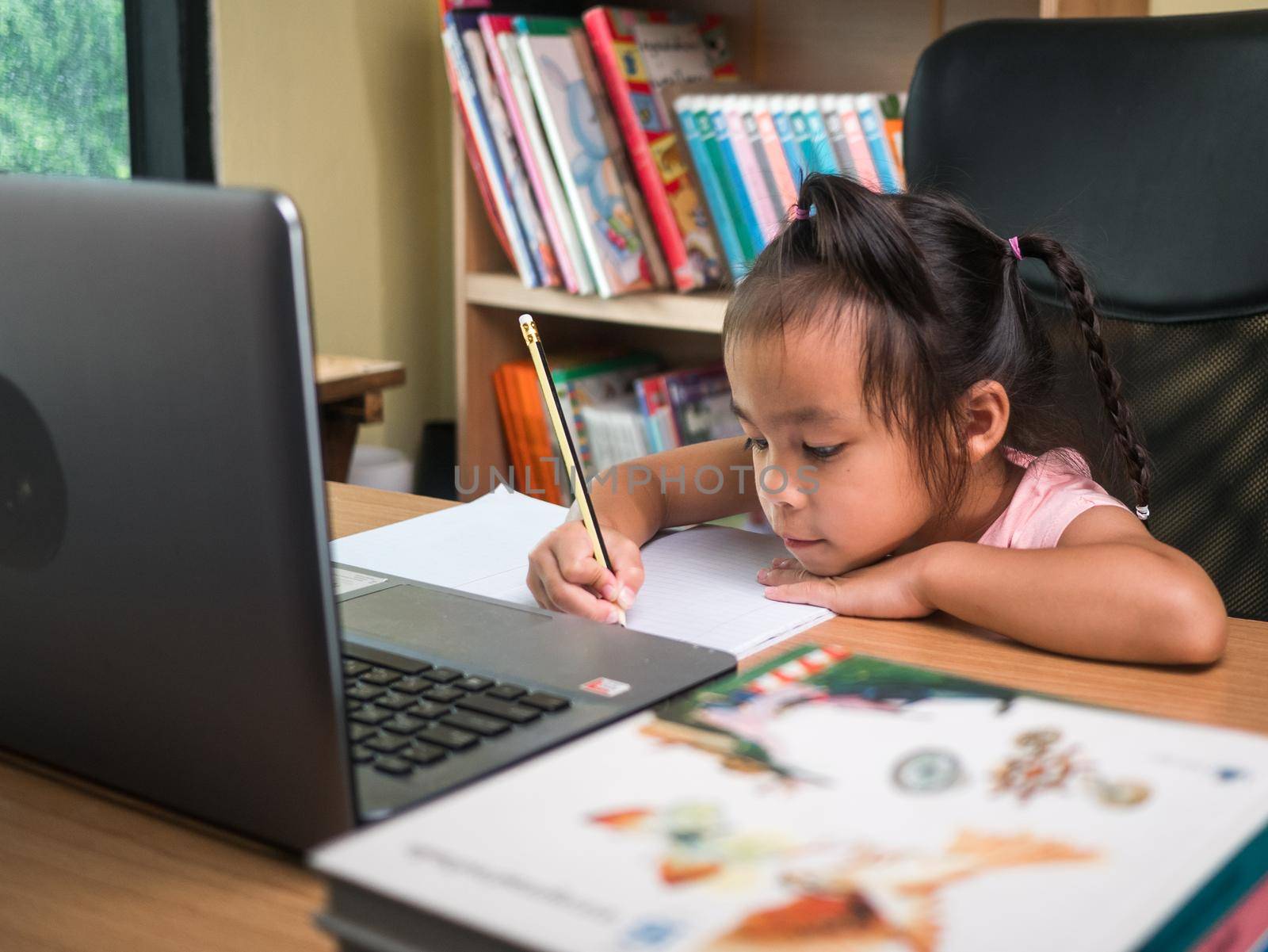 Cute little schoolgirl studying homework math during her online lesson at home, social distancing during the coronavirus outbreak. Concept of online education or home schooler. by TEERASAK