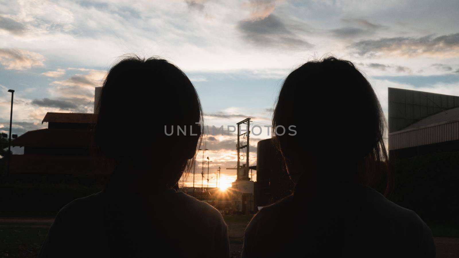 Two sibling sisters eating sweet tasty ice cream outdoors at sunset. Two happy young kid enjoy dessert during vacation holiday in the park. by TEERASAK