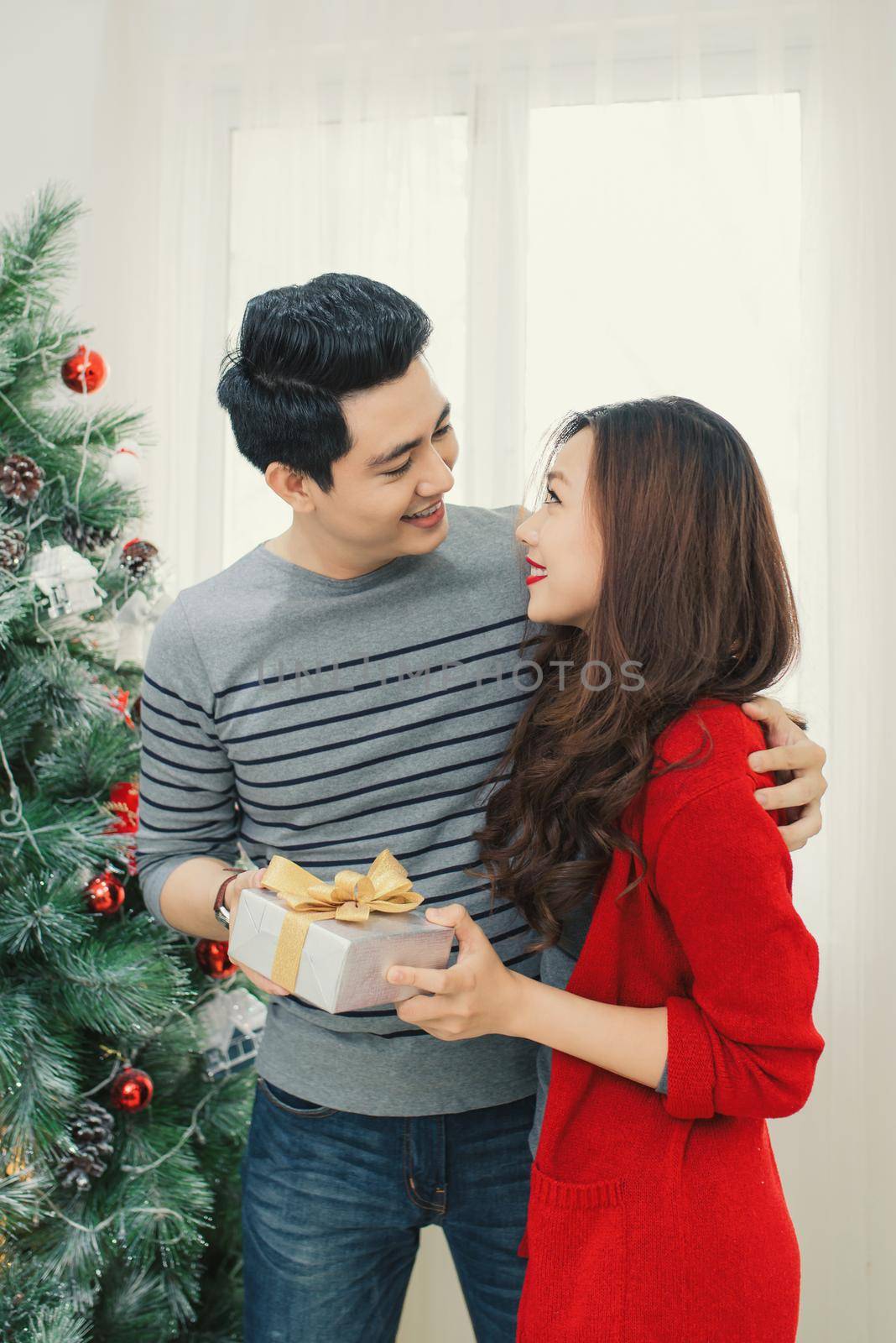 Christmas Asian Couple. A handsome man giving her girlfriend/wife a gift at home celebrating New Year People by makidotvn