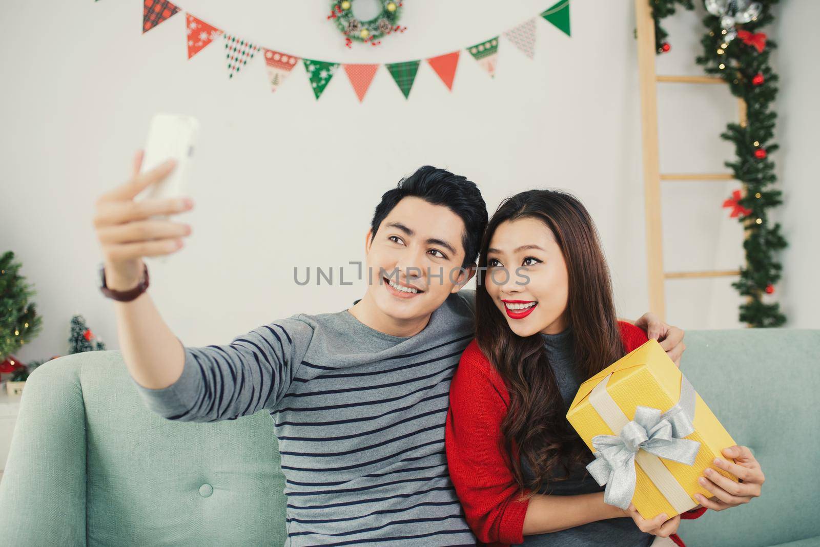 Christmas Asian Couple. A handsome man giving her girlfriend/wife a gift at home celebrating New Year People by makidotvn