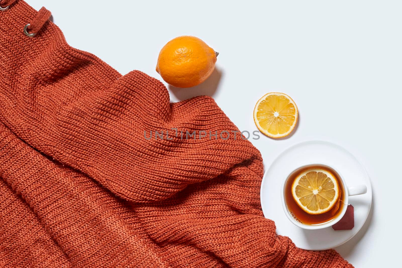 Autumn background with tea and knitted sweater on white background. Hot herbal lemon tea with orange warming pullover on white background. Fall background
