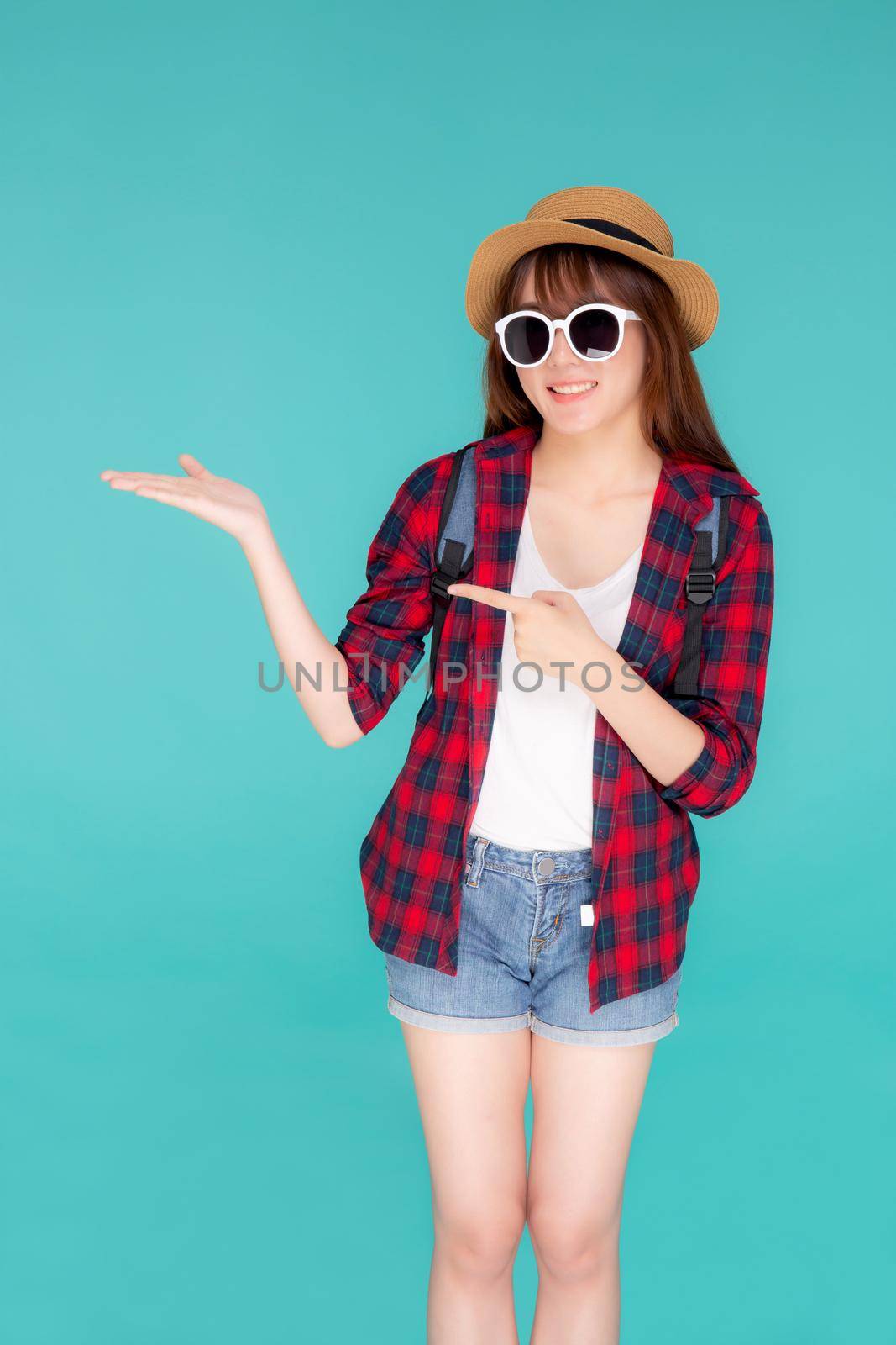 Beautiful portrait young asian woman wear sunglasses and hat smile and enjoy in summer gesture presenting and pointing something isolated on blue background, tourist girl in vacation travel concept. by nnudoo