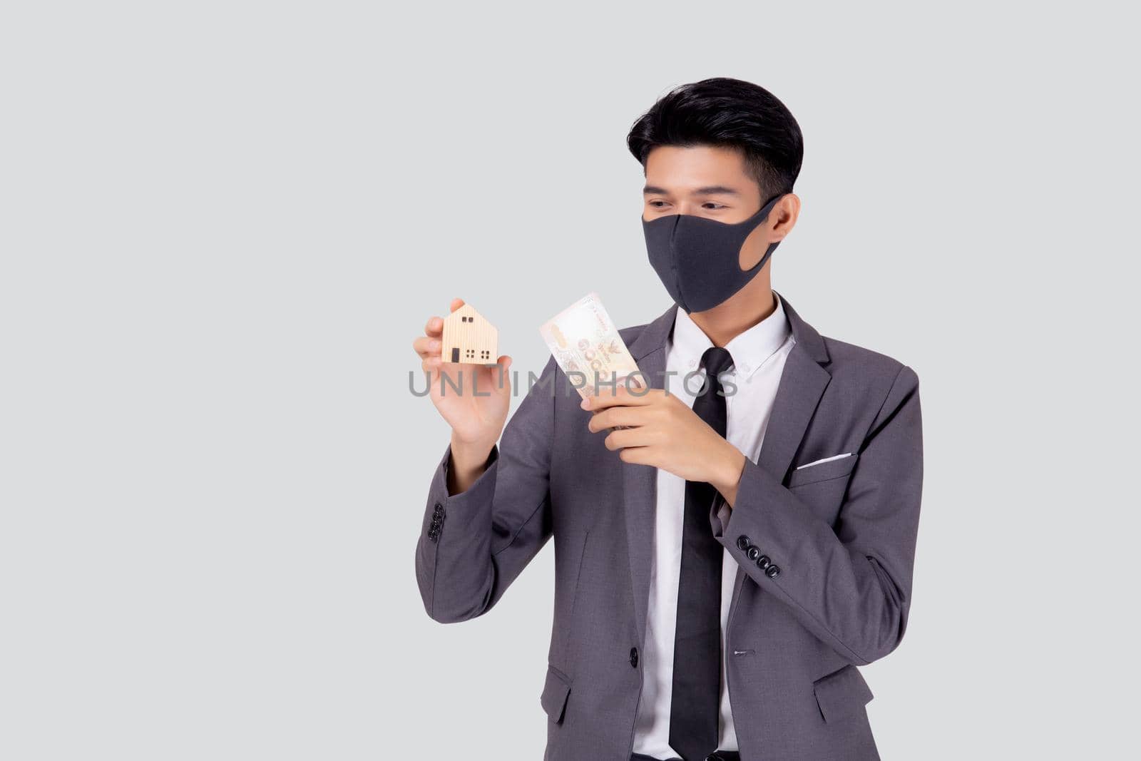 Young asian businessman in face mask holding money Thai and home isolated on white background, pandemic and crisis of economic, business man and investment property during disease covid-19. by nnudoo
