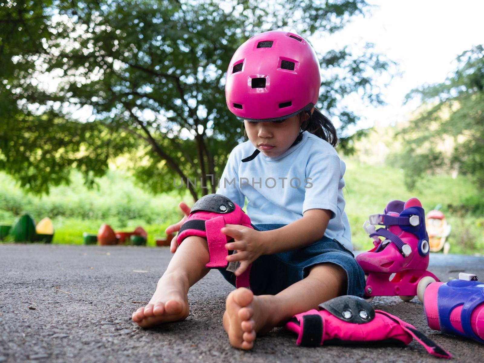 Cute little girl wearing protection pads and safety helmet practicing to roller skate on the street in the park. Active outdoor sport for kids. by TEERASAK