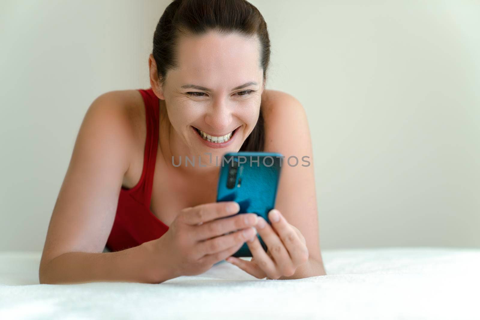 Young woman is talking on phone video camera with smile on her face lying on bed at home.