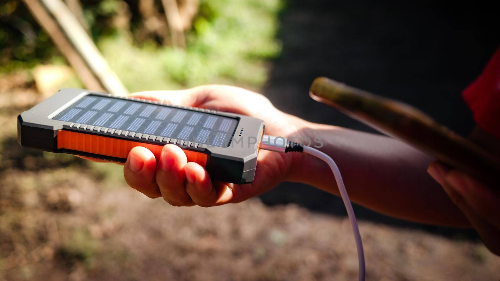 A rechargeable mobile power pack with solar panels in young female traveler's hands, close-up. Connected to and charging a mobile, tablet or smart phone. by TEERASAK