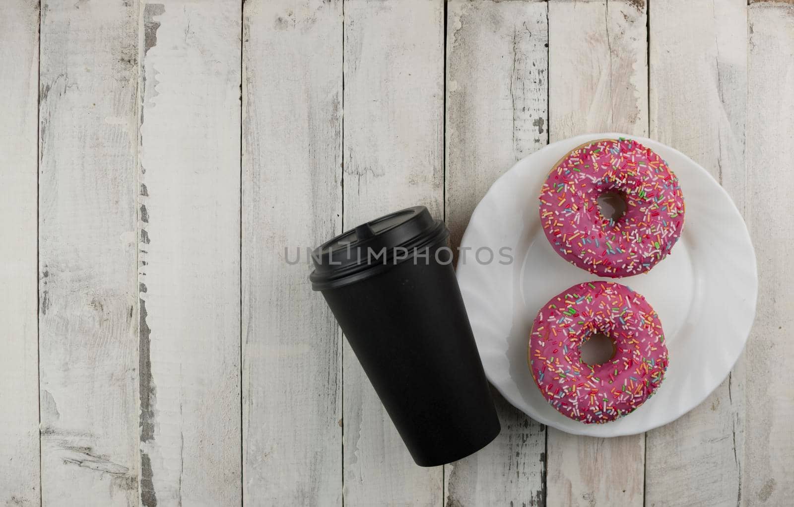 Donut on a plate and  disposable cup of coffee on a wooden table. Photo of sweets. Top view. Copy space. Mock-up 