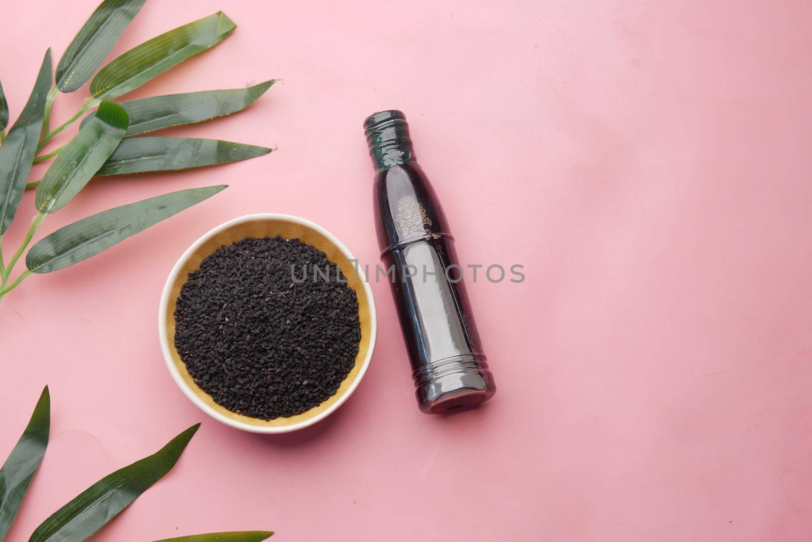 Black Cumin in a container with oil in a jar on pink