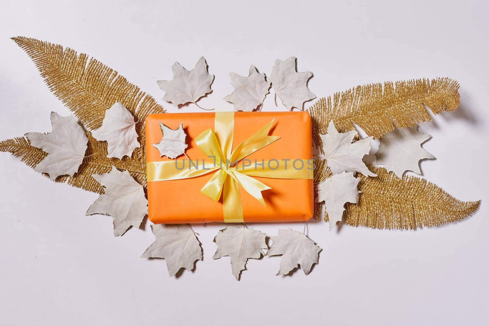 Gift boxes and fall leaves on white background. Creative lay out of autumn leaves and orange present boxes from above. Top view