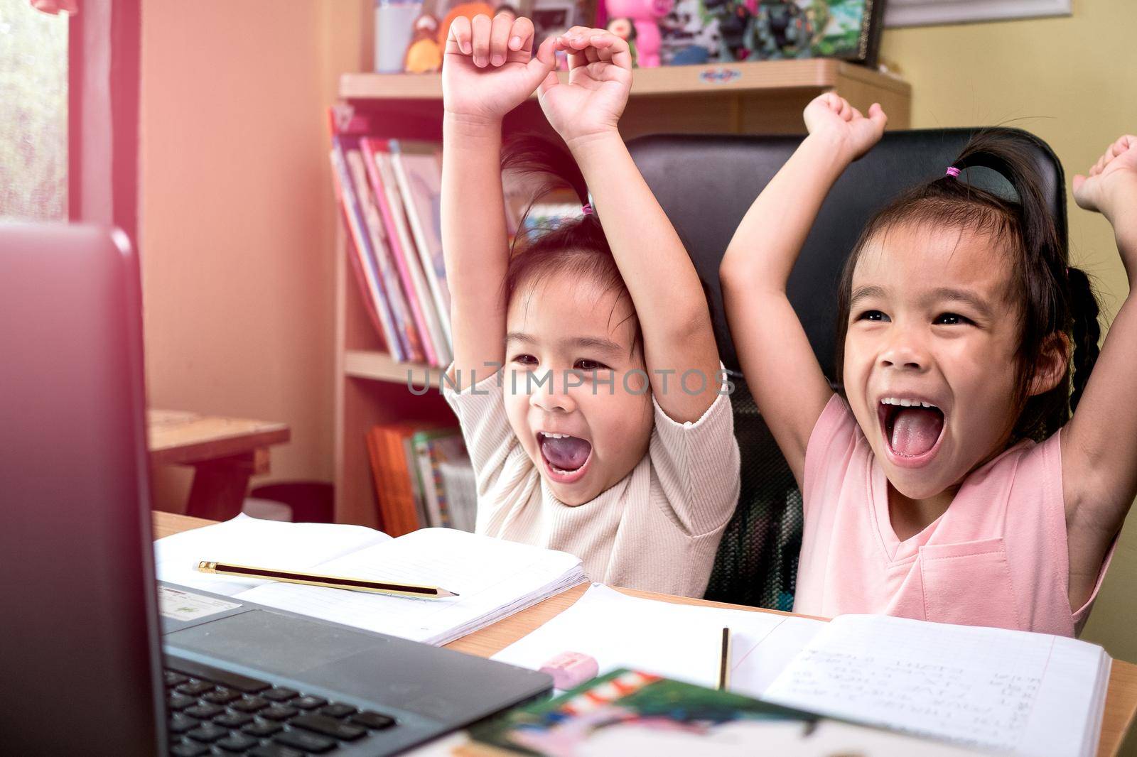 Two little schoolgirls studying homework math during her online lesson at home, social distancing during the coronavirus outbreak. Concept of online education or home schooler. by TEERASAK