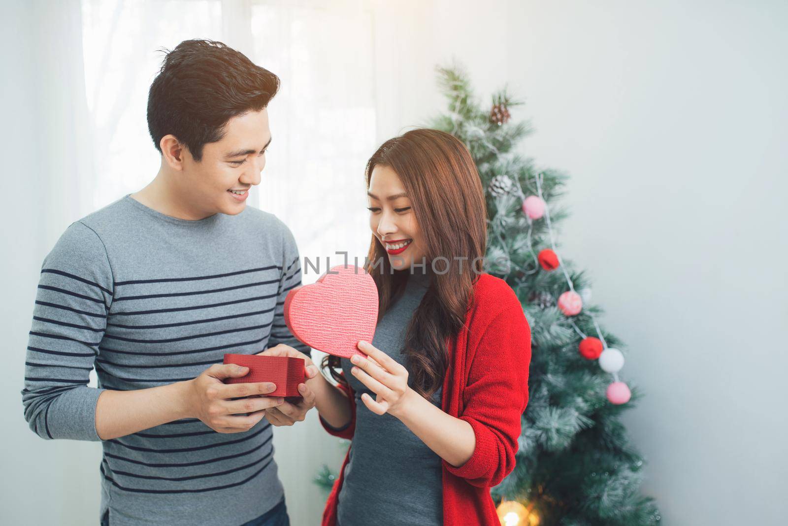 Christmas Asian Couple. A handsome man giving her girlfriend/wife a gift at home celebrating New Year People by makidotvn